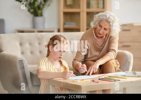 Warm getönte Porträt von älteren Frau Babysitting niedlich rothaarig Mädchen und Zeichnung zusammen, während im gemütlichen Wohnzimmer sitzen Stockfoto