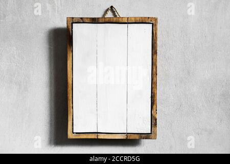 Weißes leeres Holzbrett, das an einer grauen Betonwand hängt. Platz für Logo, Zeichen oder Text. Stockfoto