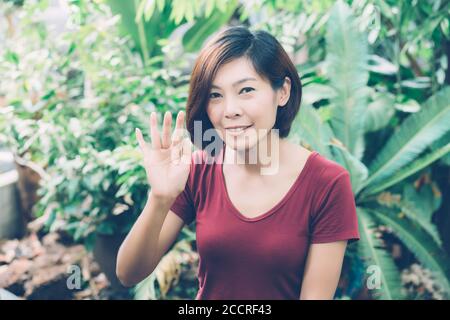 Schönes Porträt junge asiatische Frau lächelnd winkende Hand im Garten zu Hause, freundliches Mädchen und Ausdruck positive Emotion, Hallo und Gruß, ein Stockfoto