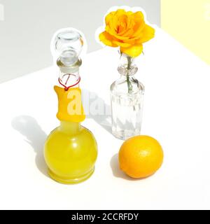 Flasche italienisches Limoncello, Zitrone und gelbe Rose. Modernes minimalistisches Stillleben auf geometrischem Hintergrund mit Sonnenlicht und Schatten. Stockfoto