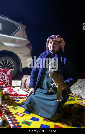 Saudi-arabischer Mann hält Falken in der Hand in der Wüste Nacht. Al-Sarar, Saudi-Arabien. Stockfoto