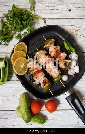 Draufsicht auf Hähnchenkebabs auf einer schwarzen Pfanne mit Gemüse und Gewürze Stockfoto