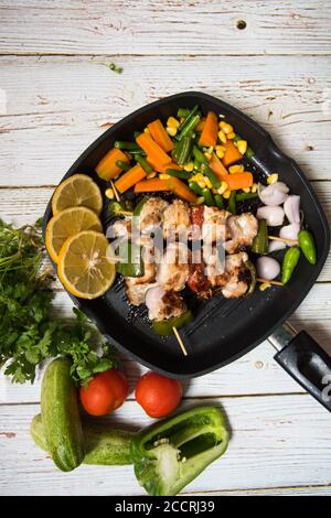 Draufsicht auf Hähnchenkebabs auf einer schwarzen Pfanne mit Gemüse und Gewürze Stockfoto