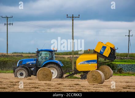 Landarbeiter fährt Tracto mit Heupresse im Erntefeld, East Lothian, Schottland, Großbritannien Stockfoto