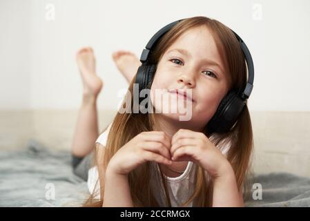 Ein Mädchen im Vorschulalter hört Musik auf ihrem Bett und dummt sich herum, schaut auf die Kamera. Stockfoto