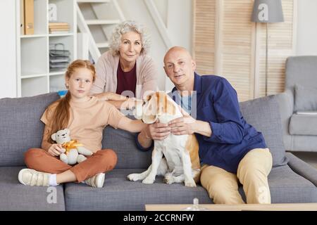 Warmes Porträt von rothaarigen Mädchen mit Großeltern sitzen auf Couch und spielen mit Hund in gemütlichen Hause Stockfoto