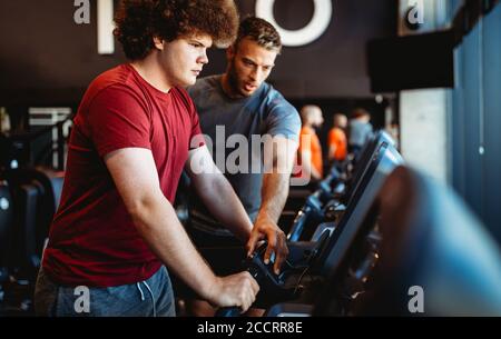 Übergewichtiger junger Mann trainiert mit persönlichem Trainer die Sporthalle Stockfoto