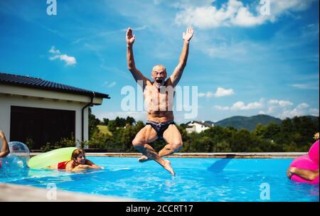 Gruppe von fröhlichen Senioren im Schwimmbad im Freien im Hinterhof, springen. Stockfoto