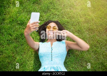 Draufsicht auf junge afroamerikanische Mädchen auf Gras liegen Und Selfie mit dem Smartphone Stockfoto