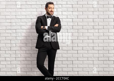 Schöner Mann in einem schwarzen Anzug mit Fliege lehnend Auf einer weißen Ziegelwand Stockfoto