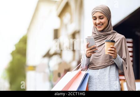 Fröhliche arabische Mädchen in Hijab mit Einkaufstaschen mit Telefon Stockfoto