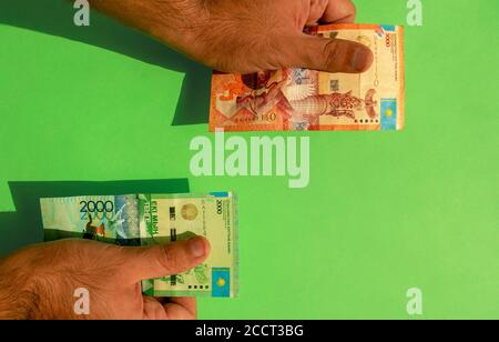 Kasachische Landeswährung. Geldscheine. Mann Hände halten kasachische Tenge Banknoten auf grünem Hintergrund. Hände mit Tenge Papiergeld. KZT Stockfoto