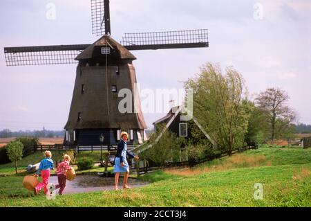 Mutter und Kinder mit Körben zu Fuß nach Hause Weg in Holland in der Nähe von Windmühle und Kanal Stockfoto