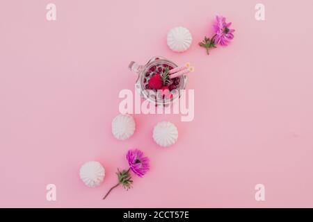 Frucht-Smoothie mit Strohhalmen, Marshmallow und Blumen auf rosa Hintergrund. Flach liegend. Draufsicht Stockfoto