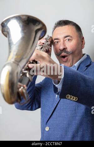Ein Mann, dunkel, kurze Haare, einen langen Schnurrbart auf der Schulter, hält eine Bassklarinette. Looks Surrised Studio, heller Hintergrund. Hochwertige Fotos Stockfoto