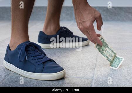 Anonymer Mann, lässig gekleidet, mit blauen Sneakers, der eine Dollarnote vom Boden abholt. Stockfoto