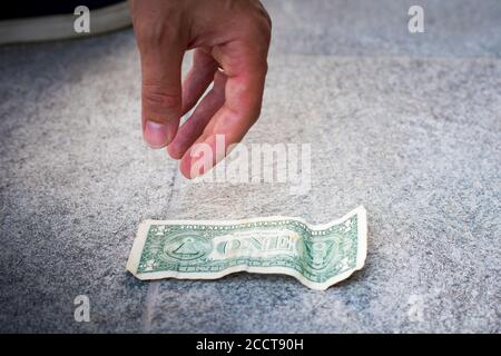 Männliche Hand, die einen Dollarschein vom Boden abholt. Stockfoto