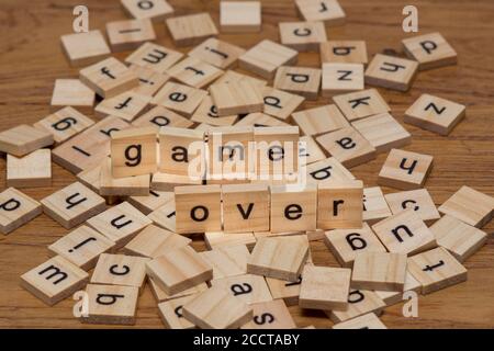 Hölzerne Buchstaben, die die Wörter "Spiel über" auf einem Hintergrund komponieren Von verstreuten Buchstaben verschüttet auf einem Holzbrett Stockfoto