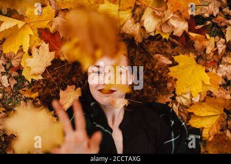 Junge glücklich Rotschopf Frau liegt auf dem Feld mit orange trocken Blätter im Herbst Stockfoto