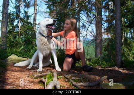 Kind blonde Mädchen posiert mit ihrem Hund (White Swiss Shepherd Dog) im Wald. Auf einem Ausflug mit einem Hund in den Wald. Auf Hund ausgerichtet Stockfoto