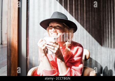 Frau lächelnd, während Sie Kaffee in der Sonne in einem trinken Cafe im Herbst Stockfoto