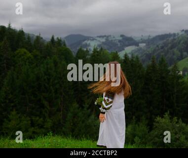 Mädchen mit losen Haaren in einer Stickerei mit einem Blumenstrauß Von Wildblumen glücklich entlang der grünen in den karpaten läuft Berge Stockfoto