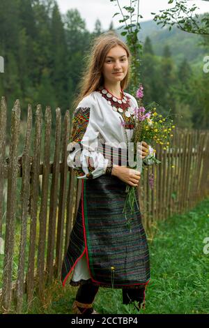 Mädchen mit lockeren Haaren mit einem Blumenstrauß steht An einem Holzzaun Stockfoto