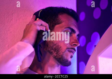 Nahaufnahme eines jungen Mannes, der nachts Musik hört. Farbleuchten Stockfoto