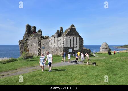 Die Menschen genießen einen warmen, sonnigen Tag, während die Sperre im 13. Jahrhundert gebauten Dunure Castle am Firth of Clyde, Ayrshire, Schottland, Großbritannien, Europa, nachlässt Stockfoto