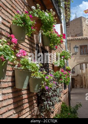 Blumentöpfe mit bunten Blumen, die an einer Ziegelwand hängen In einem spanischen Dorf Stockfoto