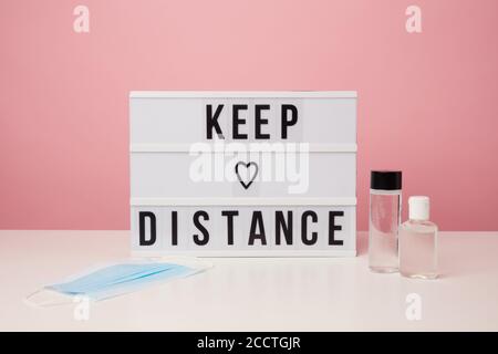 Minimales Bild von Keep Distance Sign und Handdesinfektionsmittel vor rosa Hintergrund im Studio, Kopierraum Stockfoto