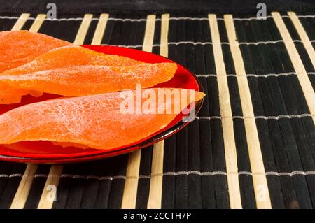 Scheiben getrocknete Mango in einer roten Untertasse auf einer Bambusmatte, Nahaufnahme. Stockfoto