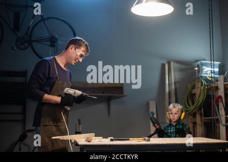 Ein erfahrener Zimmermann und sein junger Lehrling machen Holzarbeiten In ihrer Werkstatt Stockfoto