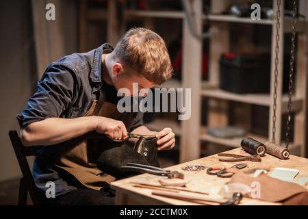 Ein junger Mann ist in der Familie Handwerk beschäftigt Herstellung von Lederschuhen in einer Werkstatt Stockfoto