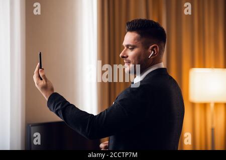 Attraktiver junger Geschäftsmann in formalwear mit einem Videoanruf auf seinem Smartphone. Ein geschäftiges Morgen in einem luxuriösen Hotel. Stockfoto
