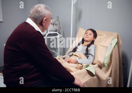 Ein kleines Mädchen, das mit einem Priester in ihrer Krankenstation spricht. Stockfoto