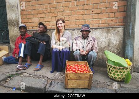 Antananarivo, Madagaskar - 24. April 2019: Junge kaukasische Frau sitzt mit lokalen Obstverkäufern in Antananarivo High Street. Trotz schlechter Wohnlage Stockfoto