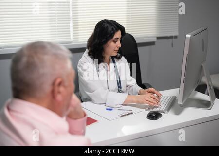 Erfahrene Krankenschwester, die die Krankengeschichte der älteren Patienten überprüft. Stockfoto