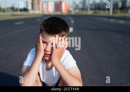 Boy sitzt auf der Fahrbahn, Sicherheit von Kindern auf der Straße, Verkehrsregeln Konzept, tödliche Bedrohung Stockfoto