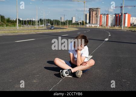 Boy sitzt auf der Fahrbahn, Sicherheit von Kindern auf der Straße, Verkehrsregeln Konzept, tödliche Bedrohung Stockfoto