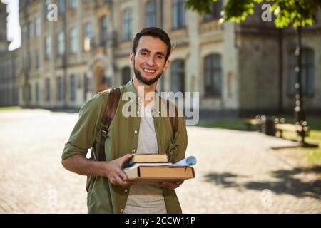 Hübscher Student, der Bücher mit beiden Händen hält Stockfoto