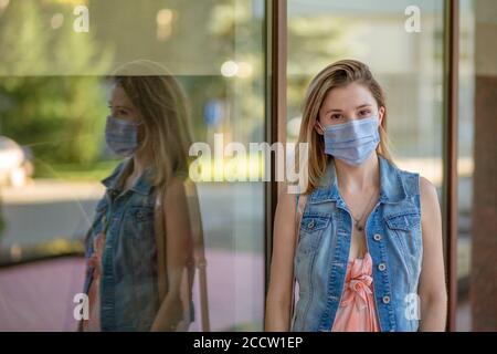 Schöne Geschäftsfrau, junge Frau, in medizinischer Schutzmaske auf ihrem Gesicht, in formeller Jacke im Freien stehend, Blick auf die Kamera. Coronavirus, viru Stockfoto