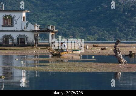 Ein Maya-Fischer in seinem Cayuco prüft seine Krabbenfalle vor einem überfluteten Gebäude in San Pedro la Laguna. Seit 2009 hat der Atitlan See in Guatemala Stockfoto