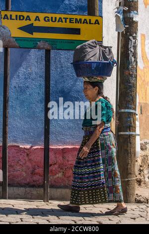 Eine ältere Tzutujil Maya Frau in traditioneller Kleidung gleicht ihre Last auf dem Kopf aus, als sie die Straße in San Pablo la Laguna, Guatemala, hinuntergeht. Beha Stockfoto