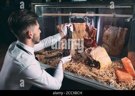 Der Kellner oder Koch bekommt trockenes Fleisch im Kühlschrank. Stockfoto