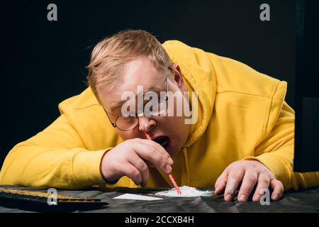 Erschöpft betrunken überdosierten Kerl in gelben Kapuzen gekleidet, schnüffelt er Drogen, während er am Tisch sitzt. Nahaufnahme Foto. Lifestyle, Freizeit Stockfoto