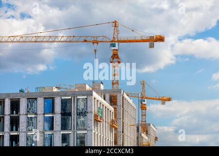 Turmkrane arbeiten auf der Baustelle eines modernen mehrstöckigen Wohngebäudes gegen einen blauen leicht bewölkten Himmel, Kopierraum. Stockfoto