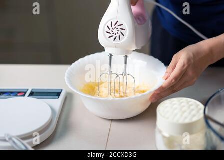 Frau mit elektrischen Mixer Zutaten für Teig von Zucker, geschlagene Eier, Butter und Mehl mischen, während Cookies in der Küche zu Hause Nahaufnahme Stockfoto