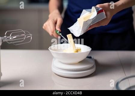 Frau, die Butter auf einer kleinen Küchenwaage während der Herstellung misst Cookies in der Küche zu Hause Nahaufnahme Stockfoto