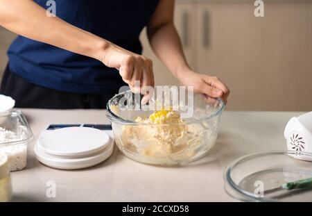 Frau, die Zutaten für Kokosnussplätzchen mischt Zuckerteig, geschlagene Eier, Butter und Mehl für die Zubereitung von hausgemachten Desserts in der Küche zu Hause aus der Nähe Stockfoto